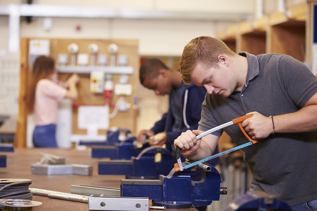 A young person cutting metal with a hand saw during a shop training session